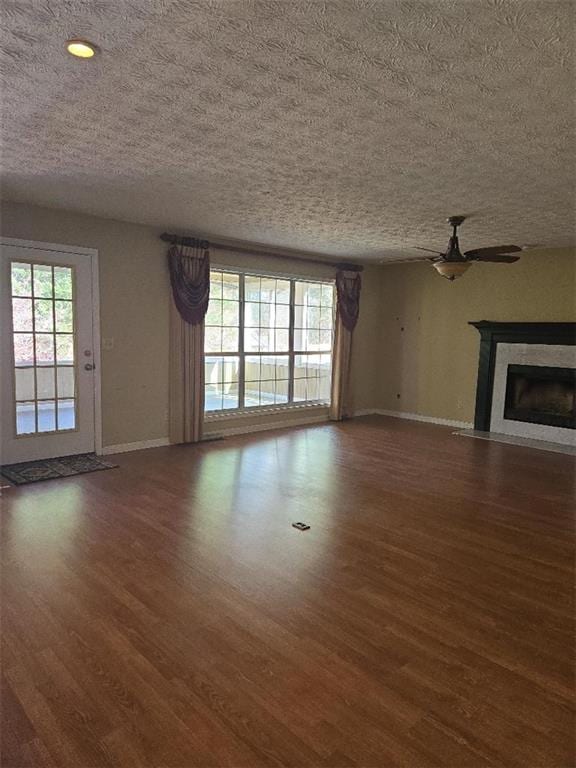 unfurnished living room with a textured ceiling, dark hardwood / wood-style floors, a wealth of natural light, and ceiling fan