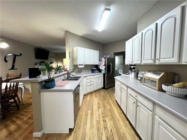 kitchen with light wood-type flooring, light countertops, fridge with ice dispenser, and a sink