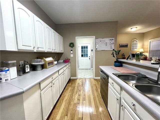 kitchen featuring light countertops, stainless steel dishwasher, a sink, light wood finished floors, and white cabinets