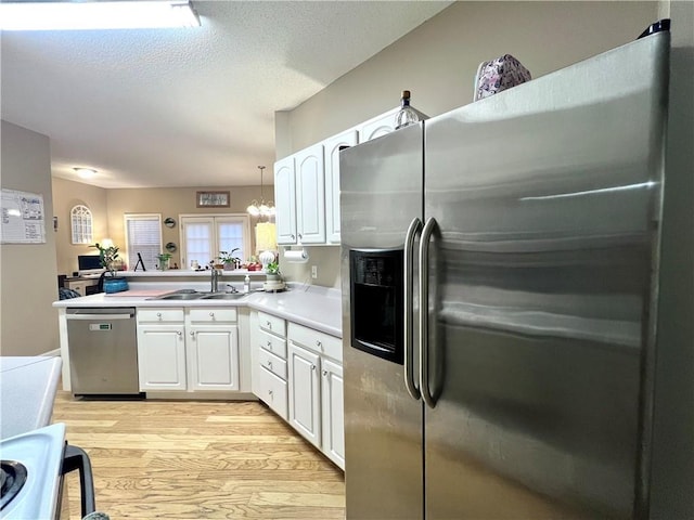 kitchen featuring light countertops, a sink, light wood-style floors, white cabinets, and appliances with stainless steel finishes