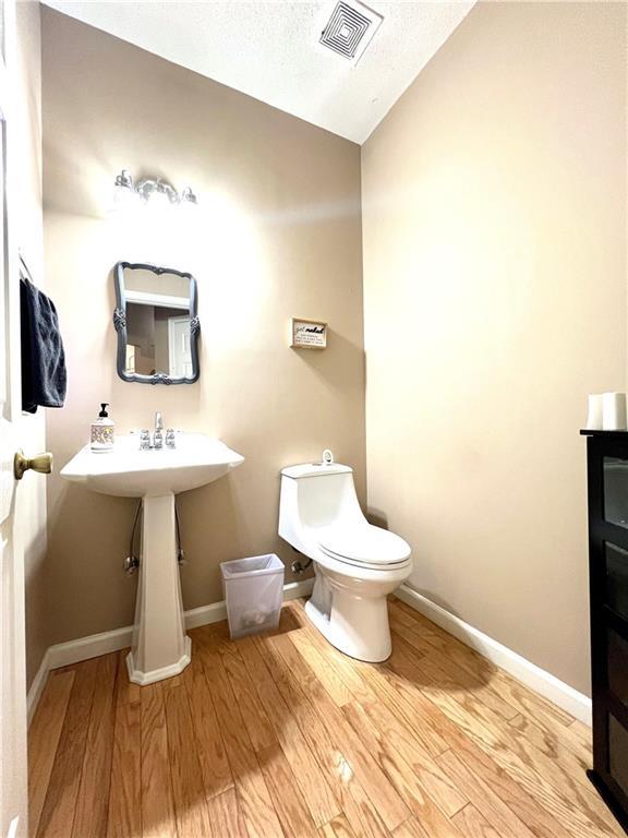 bathroom featuring toilet, wood finished floors, a textured ceiling, baseboards, and visible vents