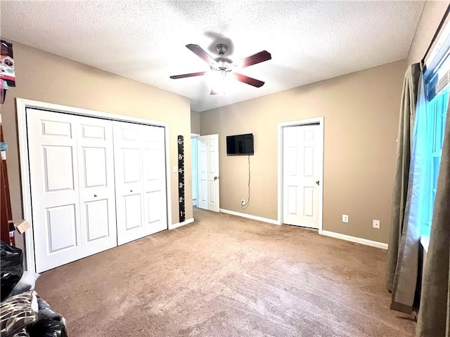 unfurnished bedroom featuring a closet, a ceiling fan, a textured ceiling, baseboards, and carpet