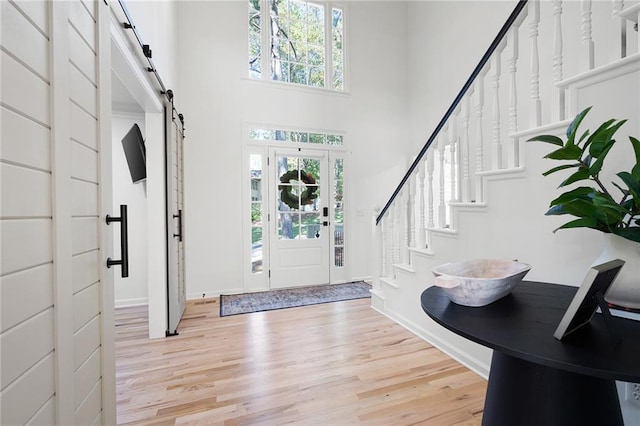 foyer featuring light hardwood / wood-style flooring, a barn door, a high ceiling, and a wealth of natural light