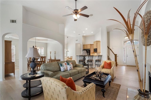 living room with light wood-type flooring, arched walkways, a towering ceiling, and ceiling fan