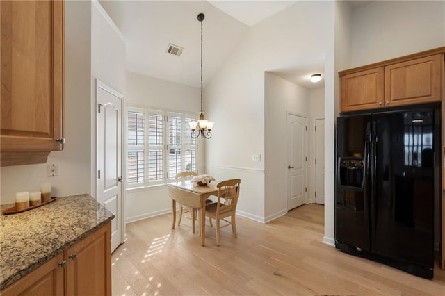 kitchen with visible vents, light stone countertops, vaulted ceiling, black fridge, and an inviting chandelier