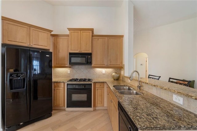 kitchen featuring light stone counters, a peninsula, arched walkways, black appliances, and a sink