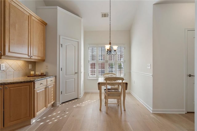 dining space featuring light wood finished floors, visible vents, baseboards, lofted ceiling, and an inviting chandelier