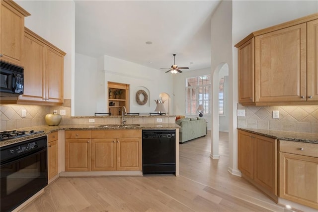 kitchen with a ceiling fan, light stone countertops, a peninsula, a sink, and black appliances