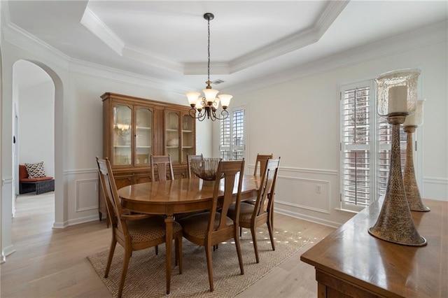 dining space with a raised ceiling, arched walkways, an inviting chandelier, and a decorative wall