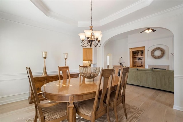 dining room featuring baseboards, arched walkways, ornamental molding, light wood-style floors, and a raised ceiling