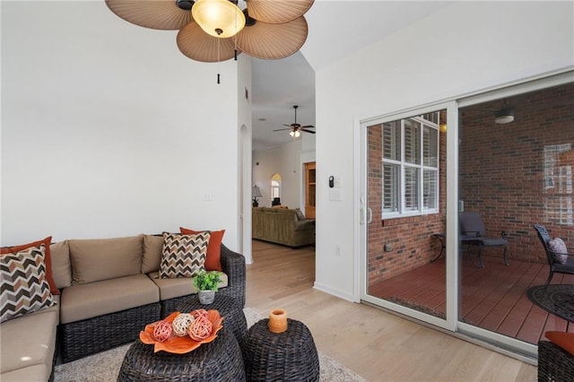 living room with light wood-style flooring, arched walkways, ceiling fan, and brick wall