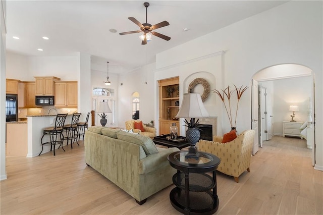 living area featuring a ceiling fan, light wood-style flooring, a fireplace, recessed lighting, and arched walkways