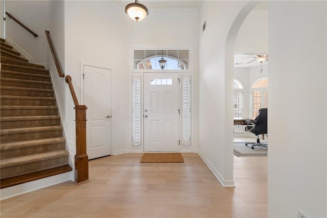 entryway featuring stairway, a ceiling fan, baseboards, light wood-style flooring, and arched walkways