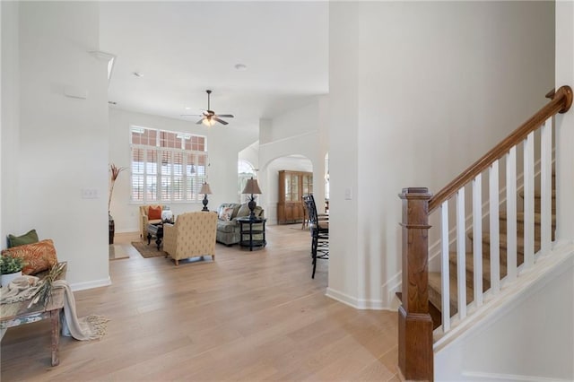 living room with baseboards, ceiling fan, stairs, light wood-type flooring, and arched walkways