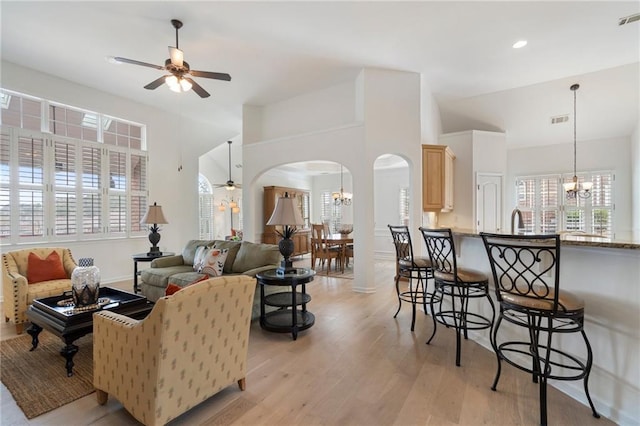 living area featuring a healthy amount of sunlight, visible vents, arched walkways, light wood-style floors, and ceiling fan with notable chandelier