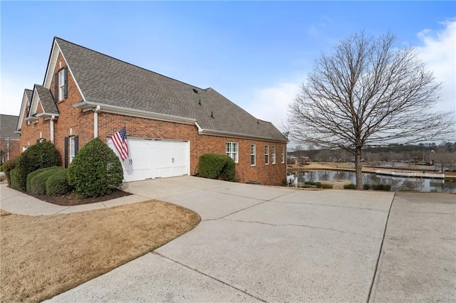 view of side of home featuring brick siding, a water view, concrete driveway, roof with shingles, and an attached garage