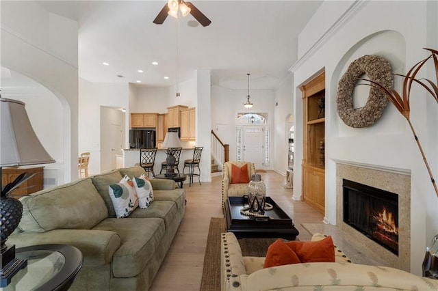 living area with arched walkways, a high ceiling, a fireplace, light wood finished floors, and ceiling fan