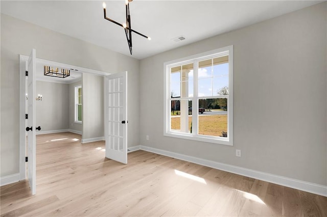 empty room featuring french doors, light hardwood / wood-style flooring, and an inviting chandelier