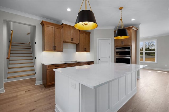 kitchen with stainless steel double oven, hanging light fixtures, light hardwood / wood-style floors, a kitchen island, and ornamental molding