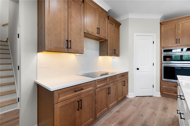 kitchen featuring black electric stovetop, light hardwood / wood-style floors, crown molding, and double oven