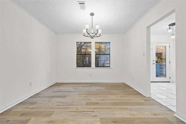 unfurnished dining area with a chandelier, a textured ceiling, light hardwood / wood-style flooring, and ornamental molding