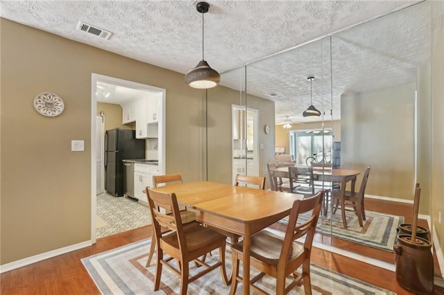 dining space with visible vents, a textured ceiling, baseboards, and wood finished floors