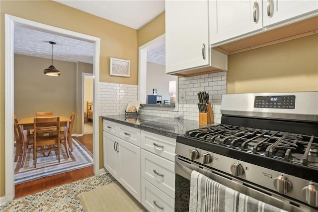 kitchen featuring decorative light fixtures, dark stone counters, white cabinets, decorative backsplash, and gas range