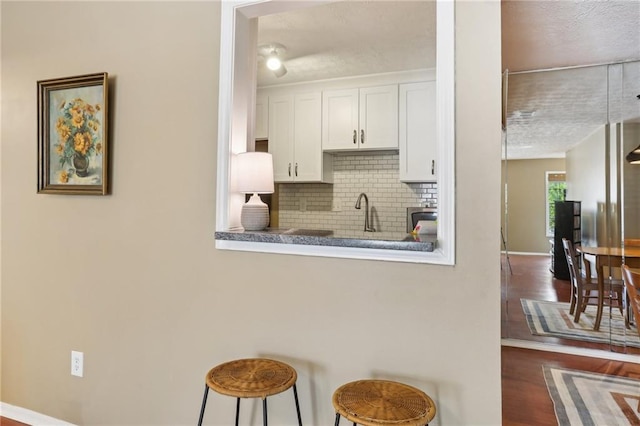 kitchen with backsplash, a kitchen breakfast bar, dark wood-style floors, white cabinets, and a textured ceiling