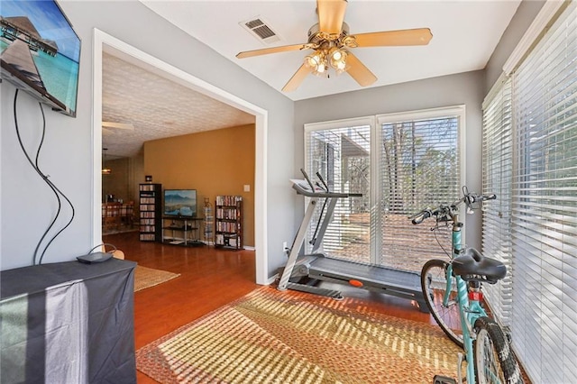 exercise area featuring ceiling fan, visible vents, baseboards, and wood finished floors