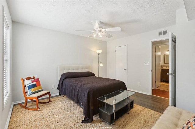 bedroom featuring visible vents, a textured ceiling, baseboards, and wood finished floors