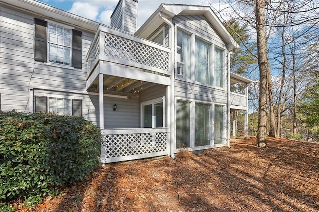 back of property featuring a balcony and a chimney