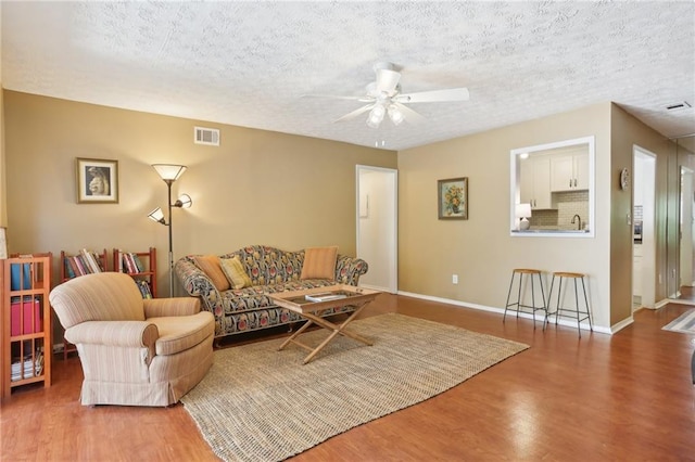 living room with a ceiling fan, wood finished floors, visible vents, and a textured ceiling