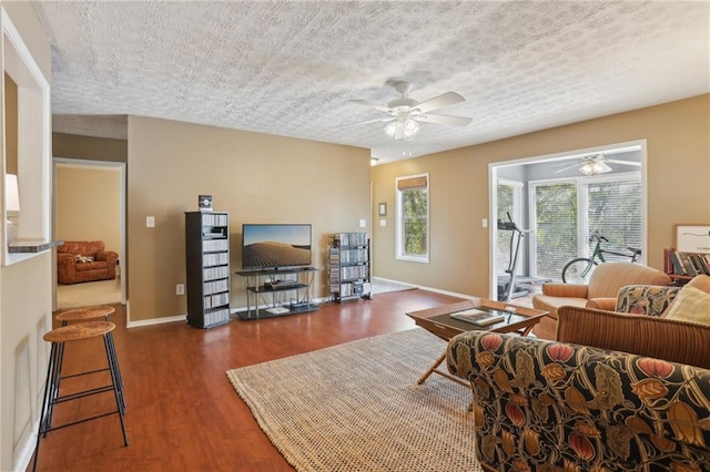 living area featuring baseboards, a textured ceiling, a ceiling fan, and wood finished floors