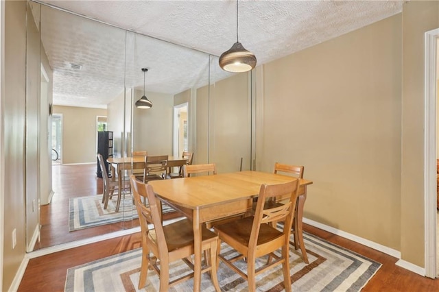 dining room with a textured ceiling, wood finished floors, visible vents, and baseboards