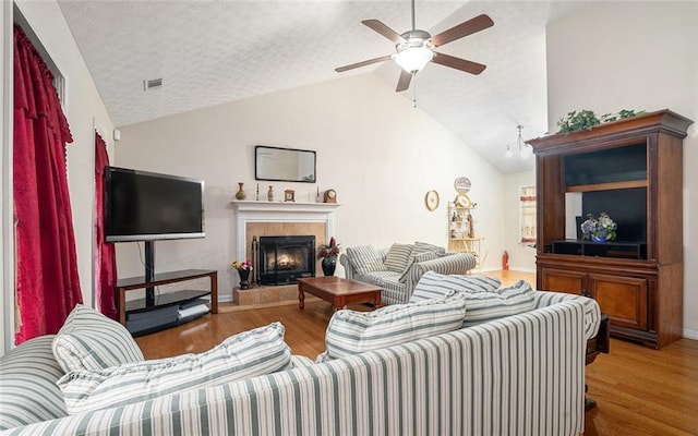 living room featuring a tile fireplace, ceiling fan, hardwood / wood-style floors, a textured ceiling, and lofted ceiling