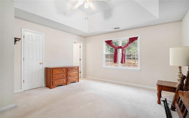 bedroom with a raised ceiling, ceiling fan, and light carpet