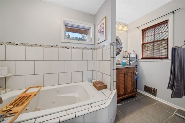 full bathroom with visible vents, tile walls, a tub with jets, tile patterned flooring, and vanity