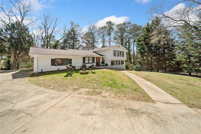 tri-level home featuring brick siding, driveway, a fire pit, and a front yard