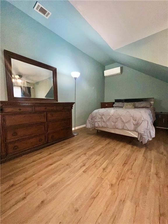 bedroom with a wall mounted air conditioner, lofted ceiling, and light hardwood / wood-style flooring