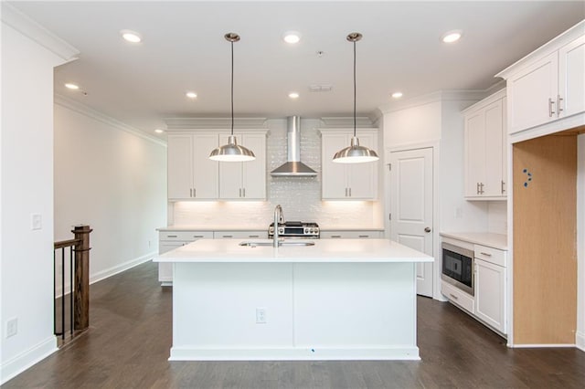 kitchen featuring baseboards, a center island with sink, wall chimney range hood, light countertops, and tasteful backsplash