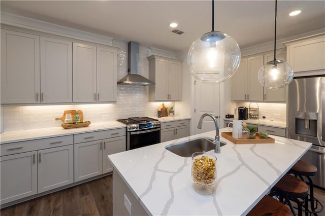 kitchen featuring wall chimney range hood, stainless steel appliances, a center island with sink, sink, and light stone counters