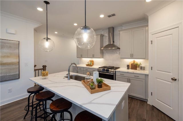 kitchen featuring a kitchen island with sink, wall chimney exhaust hood, pendant lighting, stainless steel range with gas cooktop, and light stone counters