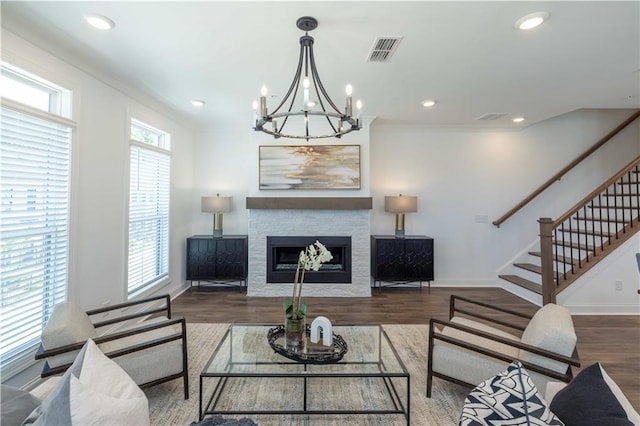 living area with a stone fireplace, visible vents, wood finished floors, stairway, and baseboards