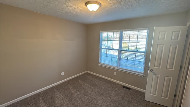 empty room with a textured ceiling and dark colored carpet