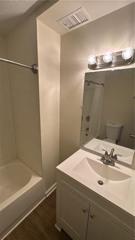 full bathroom with toilet, hardwood / wood-style floors, shower / bath combo with shower curtain, a textured ceiling, and vanity