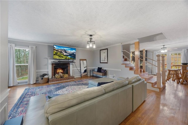 living room featuring a brick fireplace, stairway, light wood-type flooring, ornamental molding, and a textured ceiling