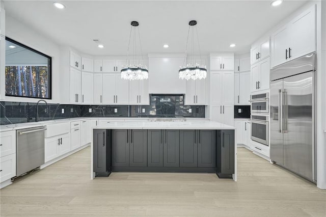 kitchen featuring white cabinets, appliances with stainless steel finishes, a kitchen island, hanging light fixtures, and light stone counters