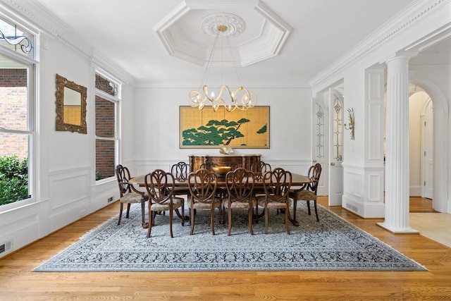 dining space featuring hardwood / wood-style flooring, decorative columns, crown molding, and a notable chandelier