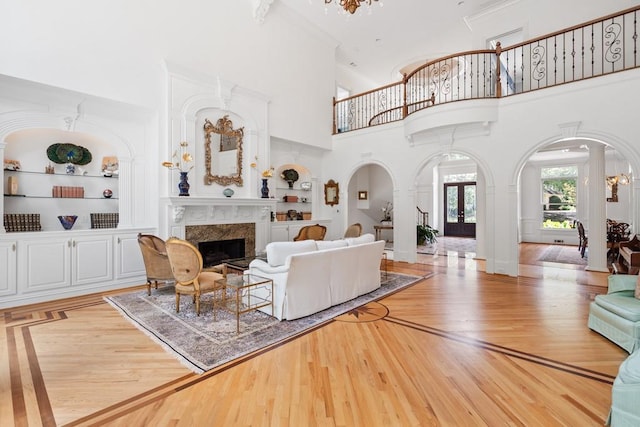 living room with built in shelves, light wood-type flooring, a premium fireplace, and a high ceiling