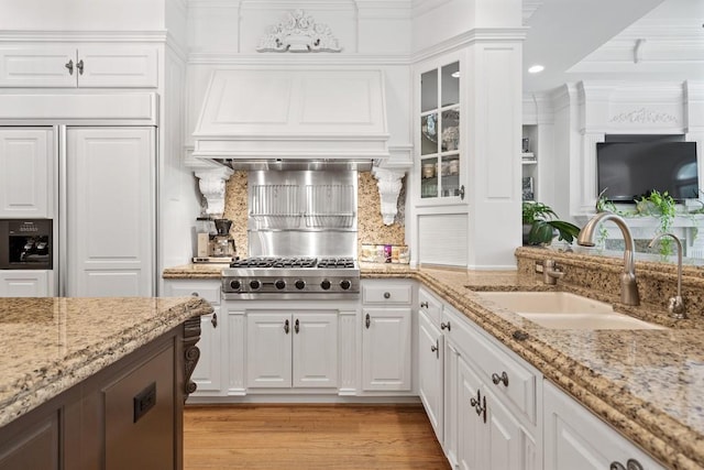 kitchen featuring white cabinetry, light stone counters, paneled built in refrigerator, light wood-type flooring, and sink